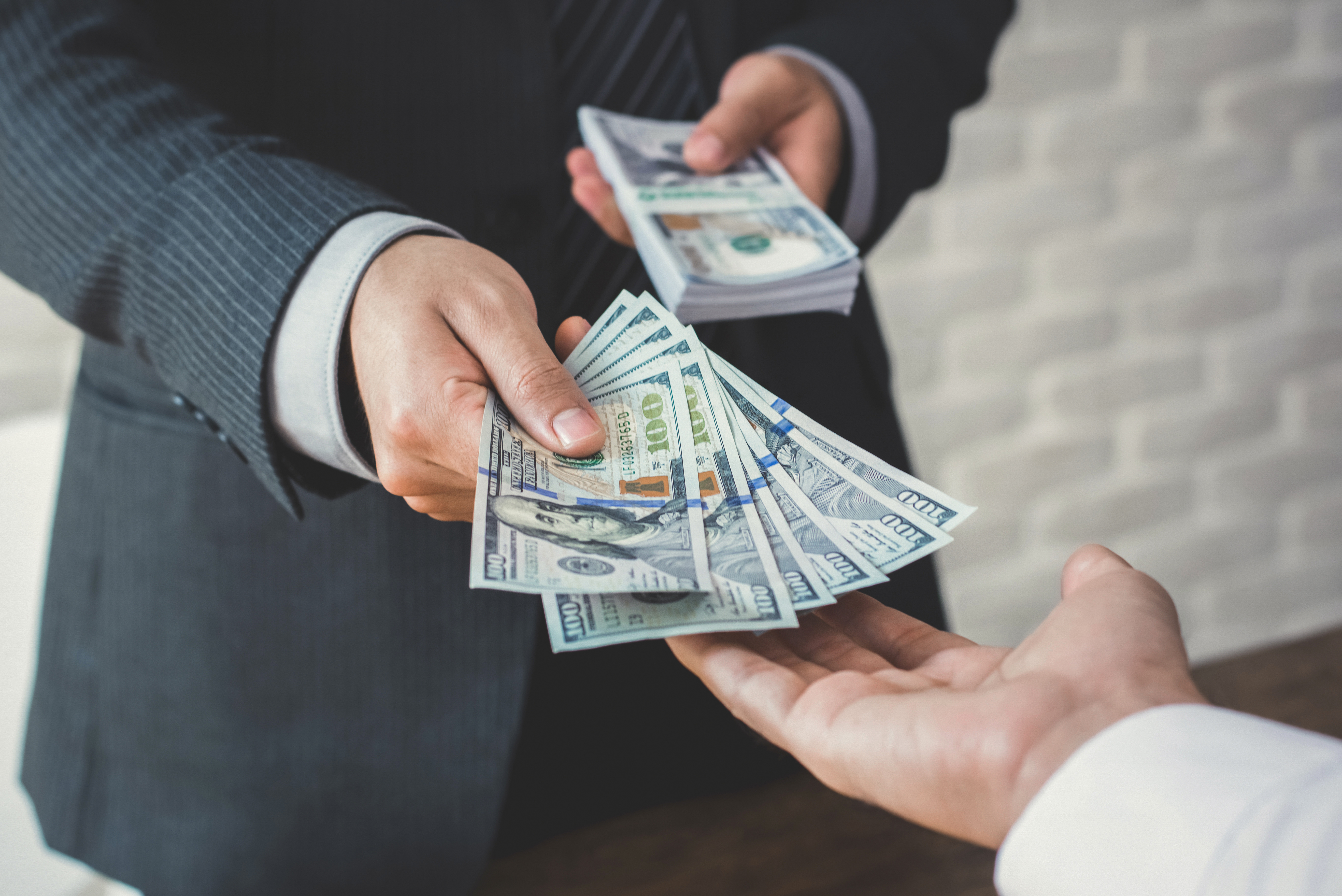 Businessman giving or paying money to a man, US dollar bills - loan,bribery and financial concepts